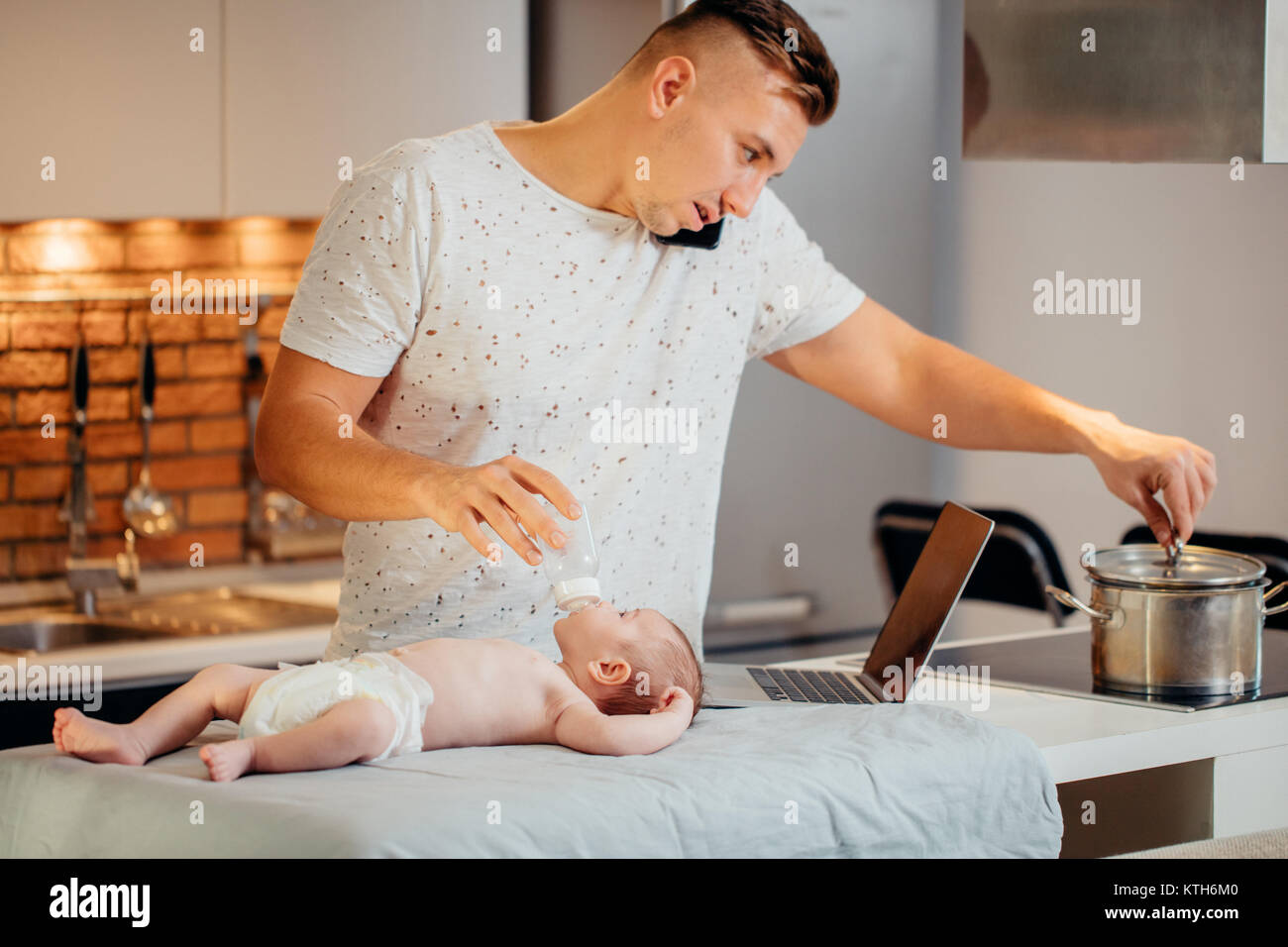 Seul papa travaille sur un ordinateur portable à la maison tout en prenant soin de son fils bébé Banque D'Images