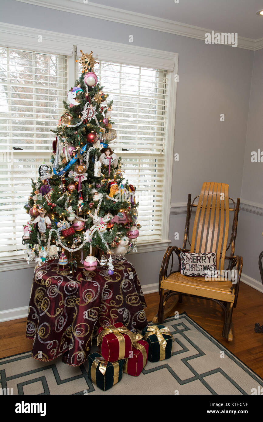 Un petit, joliment décorée d'arbres de Noël de table en face d'une fenêtre et à côté d'un fauteuil à bascule. Banque D'Images