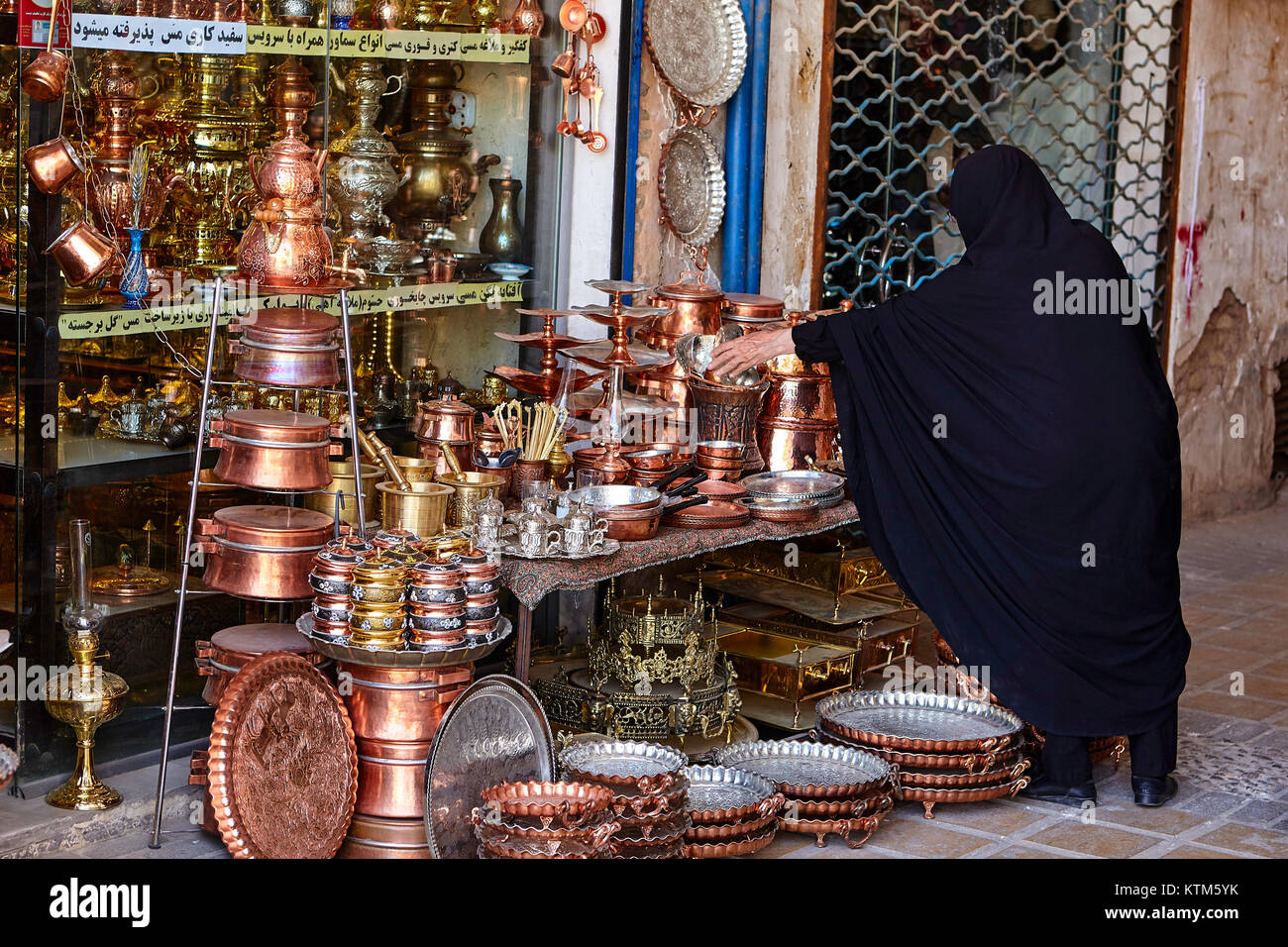 Yazd, Iran - avril 22, 2017 : une femme musulmane vêtue d'un voile religieux noir choisit un bol en métal dans l'ware shop au bazar de cuivre. Banque D'Images