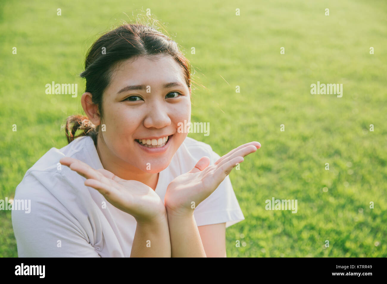Jolies jeunes asiatiques sourire innocent de l'adolescence présente son visage sur fond d'herbe verte Banque D'Images