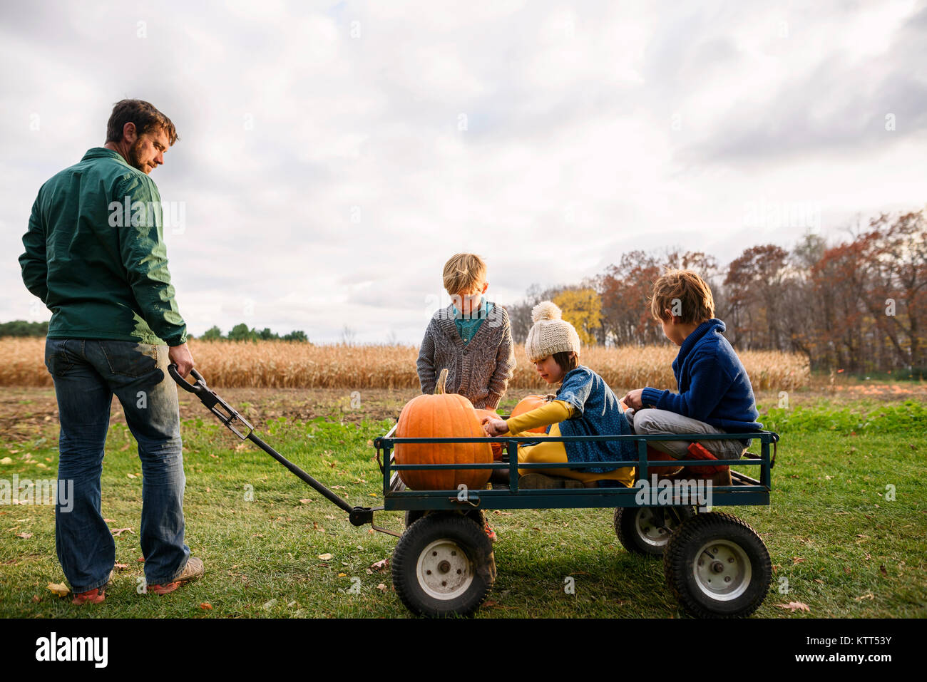 Père de trois enfants à cheval sur un wagon avec des citrouilles Banque D'Images