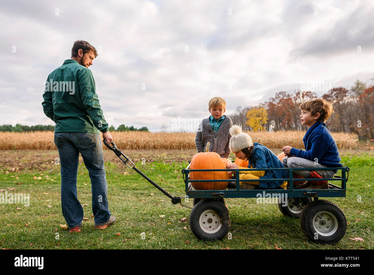 Père de trois enfants à cheval sur un wagon avec des citrouilles Banque D'Images