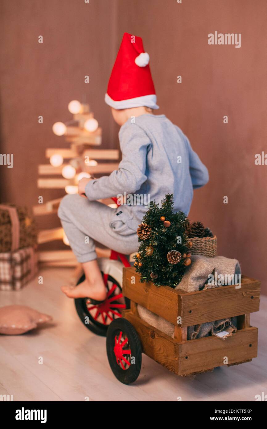 Boy wearing a santa hat ricing un tricycle avec décorations de Noël Banque D'Images