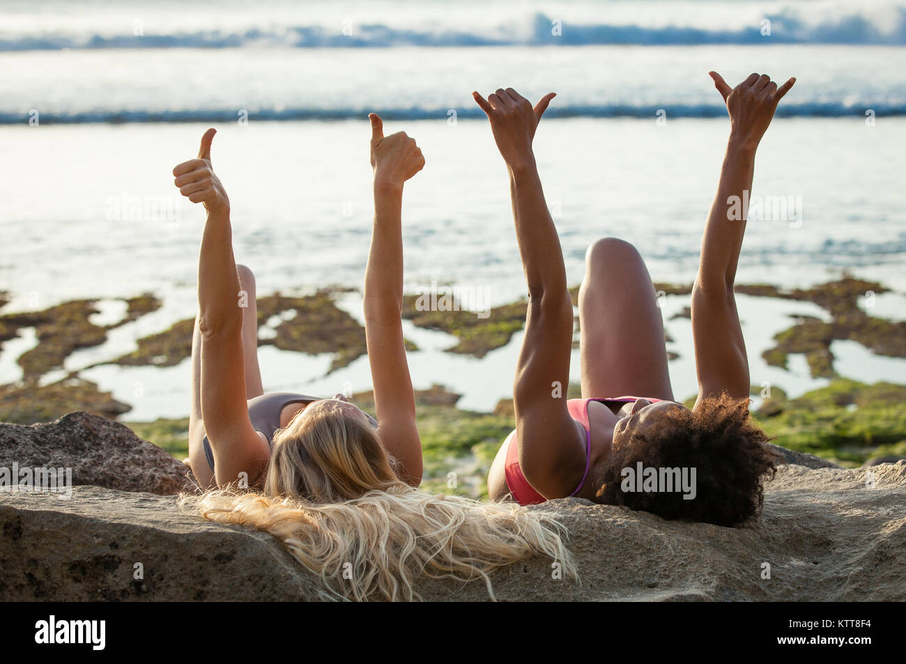 Surfer Girls accueillant des vagues avec les bras tendus et les pouces jusqu'à la plage de Balangan, Bali, Indonésie. Banque D'Images