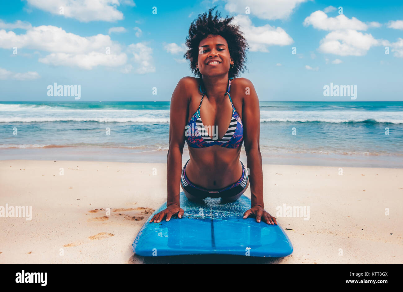 Surfer Girl avec coiffure afro smiling, couchée sur bleu surf sur la plage de sable blanc à Dreamland, Bali, Indonésie Banque D'Images