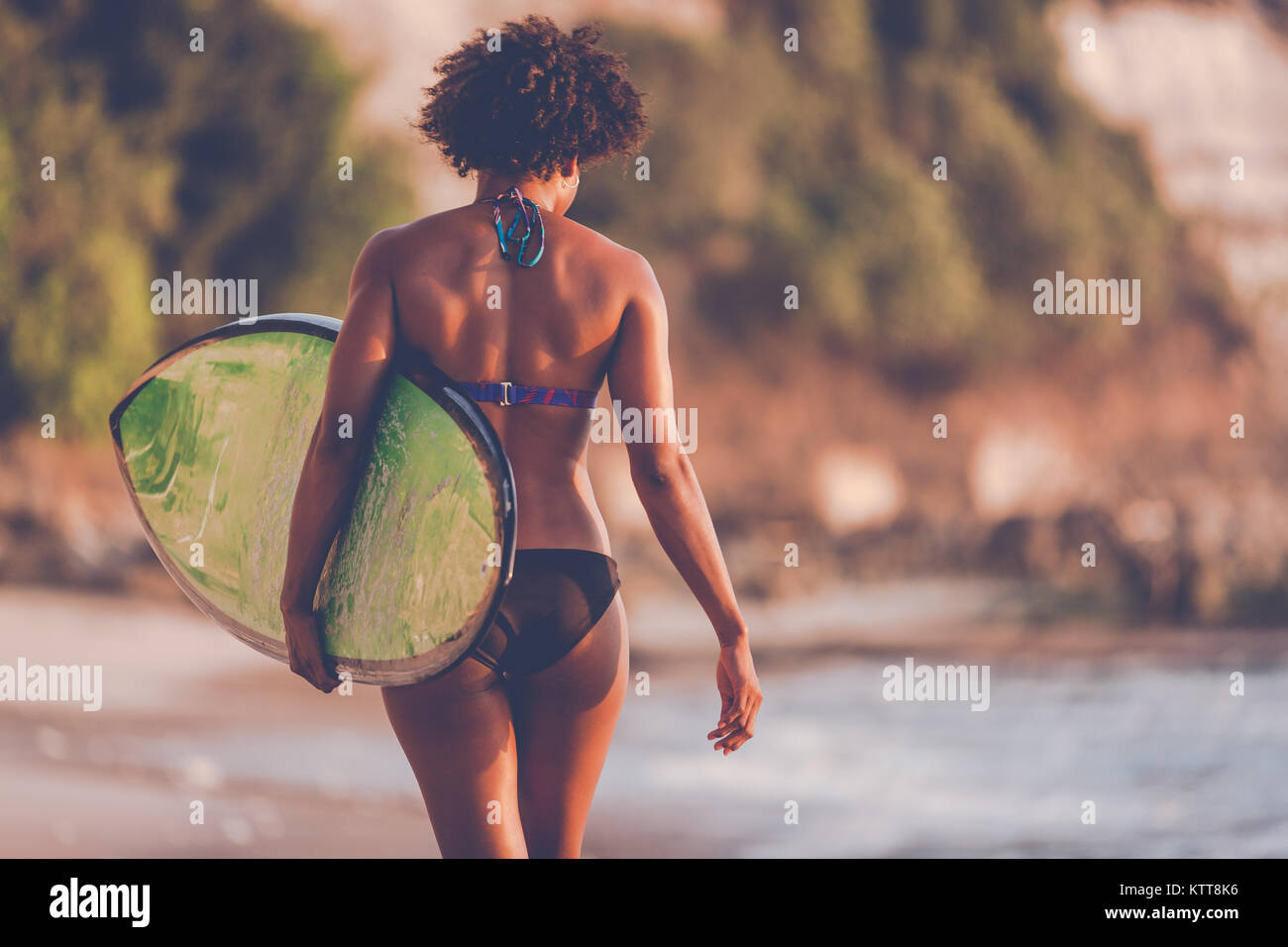 Surfer Girl avec coiffure afro walking with surfboard sur la plage au coucher du soleil Padang Padang à Bali, Indonésie Banque D'Images