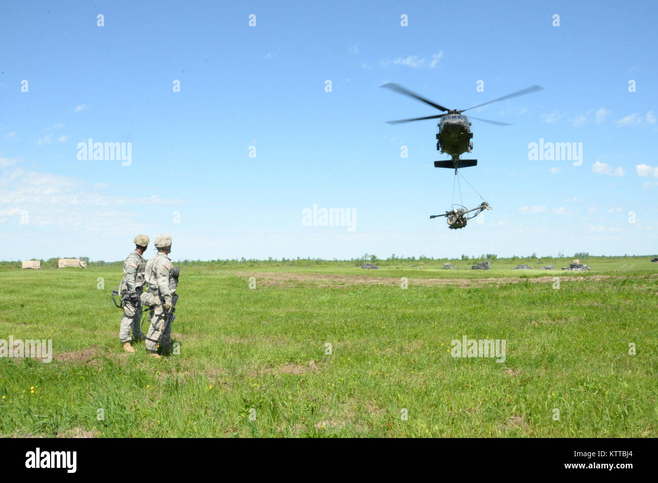 Les soldats de la Garde nationale de l'Armée américaine du 1er bataillon du 258e d'artillerie sur le terrain, regarder comme un UH-60 Black Hawk transporte un obusier M119A2 plus de Fort Drum, N.Y., 8 juin 2017. Le 258e a été la réalisation de la formation annuelle avec le 3e bataillon du 142e, Division de l'aviation, qui impliquait le transport d'obusiers. (U.S. La Garde nationale de l'armée photo de la FPC. Andrew Valenza) Banque D'Images