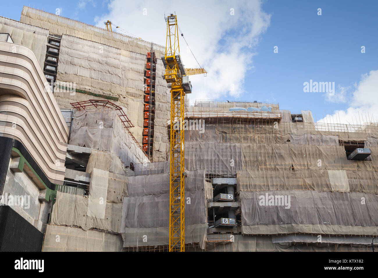 Grue à tour jaune travaille près de maison de béton avec l'échafaudage, le bâtiment est en cours de construction Banque D'Images