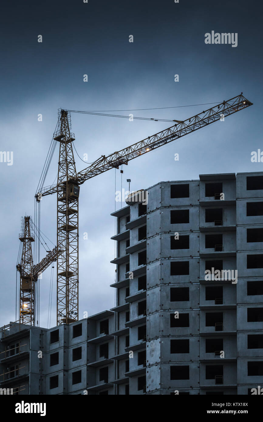 Travail de nuit les grues près de maison de béton avec carcasse windows vide, le bâtiment est en construction Banque D'Images