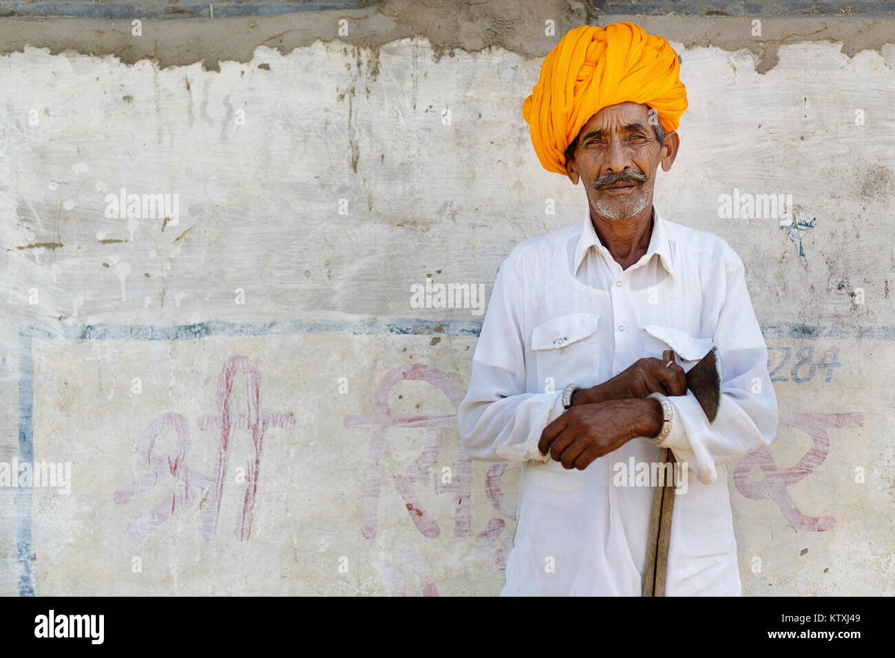 Vieil indien homme en blanc tenue le port du turban orange, debout devant un mur blanc dans un village près de Pushkar, Rajasthan, Inde. Banque D'Images