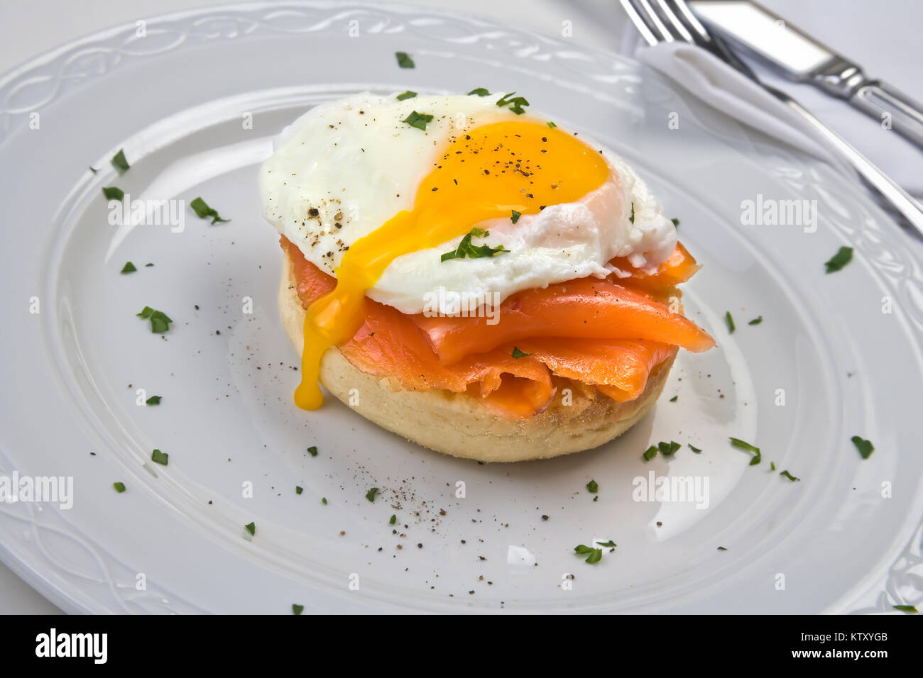 Soft œuf poché sur un muffin au saumon fumé grillé sur plaque blanche dentelle sur fond blanc Banque D'Images