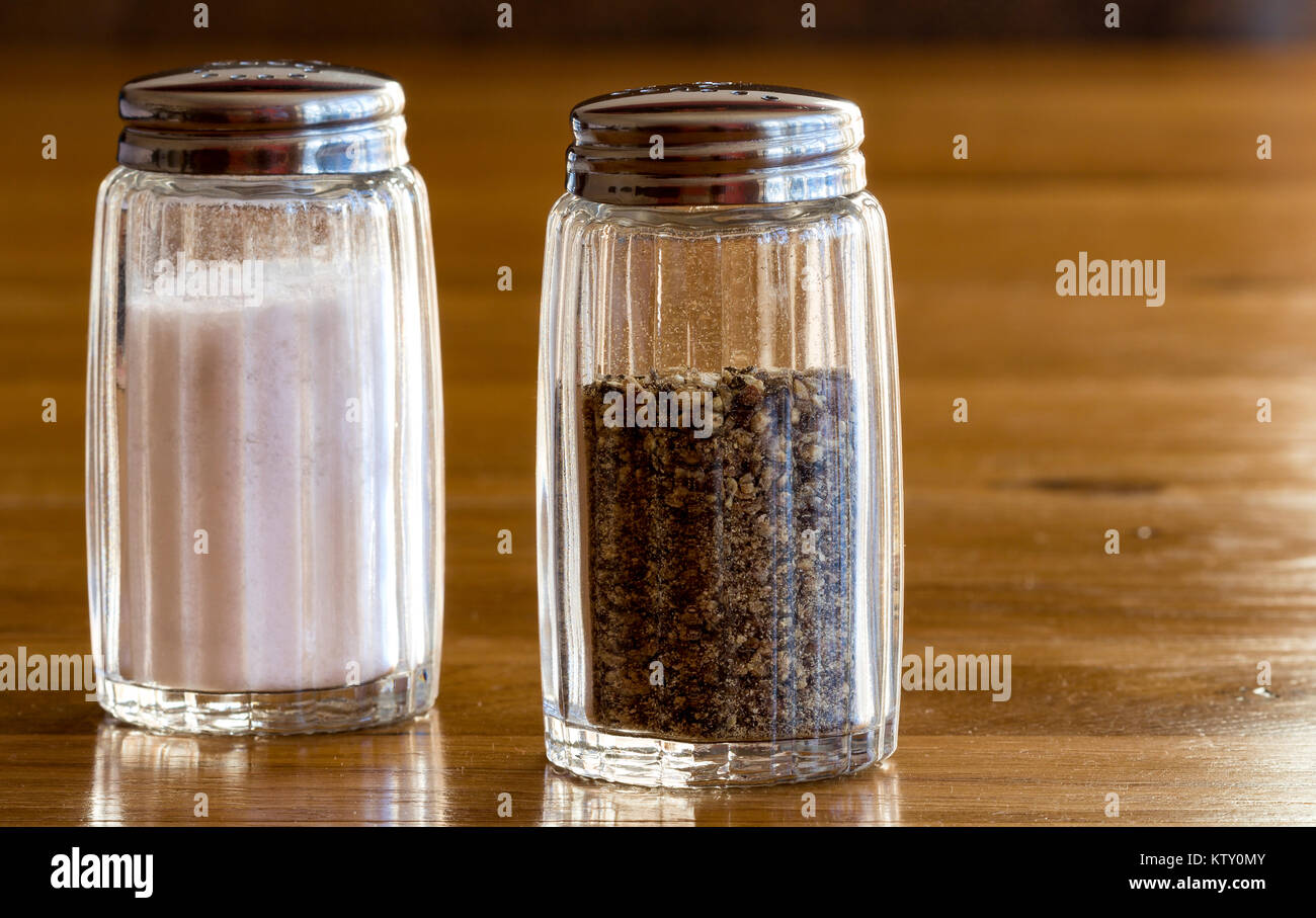 Close up de salière et poivrière en verre ou des pots de sel et de poivre sur une table en bois ,très commun coin condiments vu sur n'importe quelle table aux heures des repas Banque D'Images