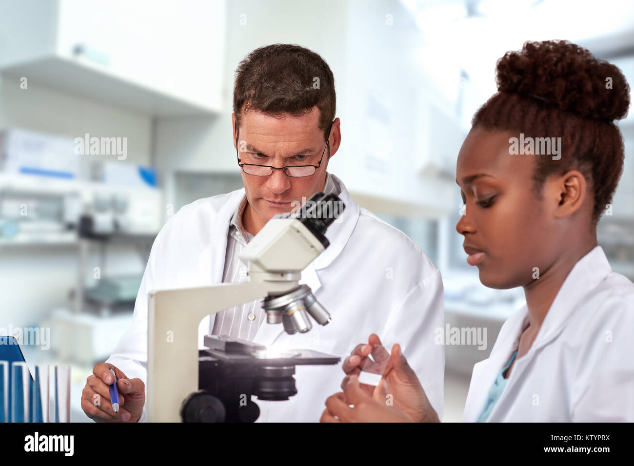 Scientifiques, cadres supérieurs de l'Afrique de l'homme de race blanche et jeune femme, travailler avec un microscope à l'installation de recherche. Shallow DOF, se concentrer sur le mans les yeux. Banque D'Images