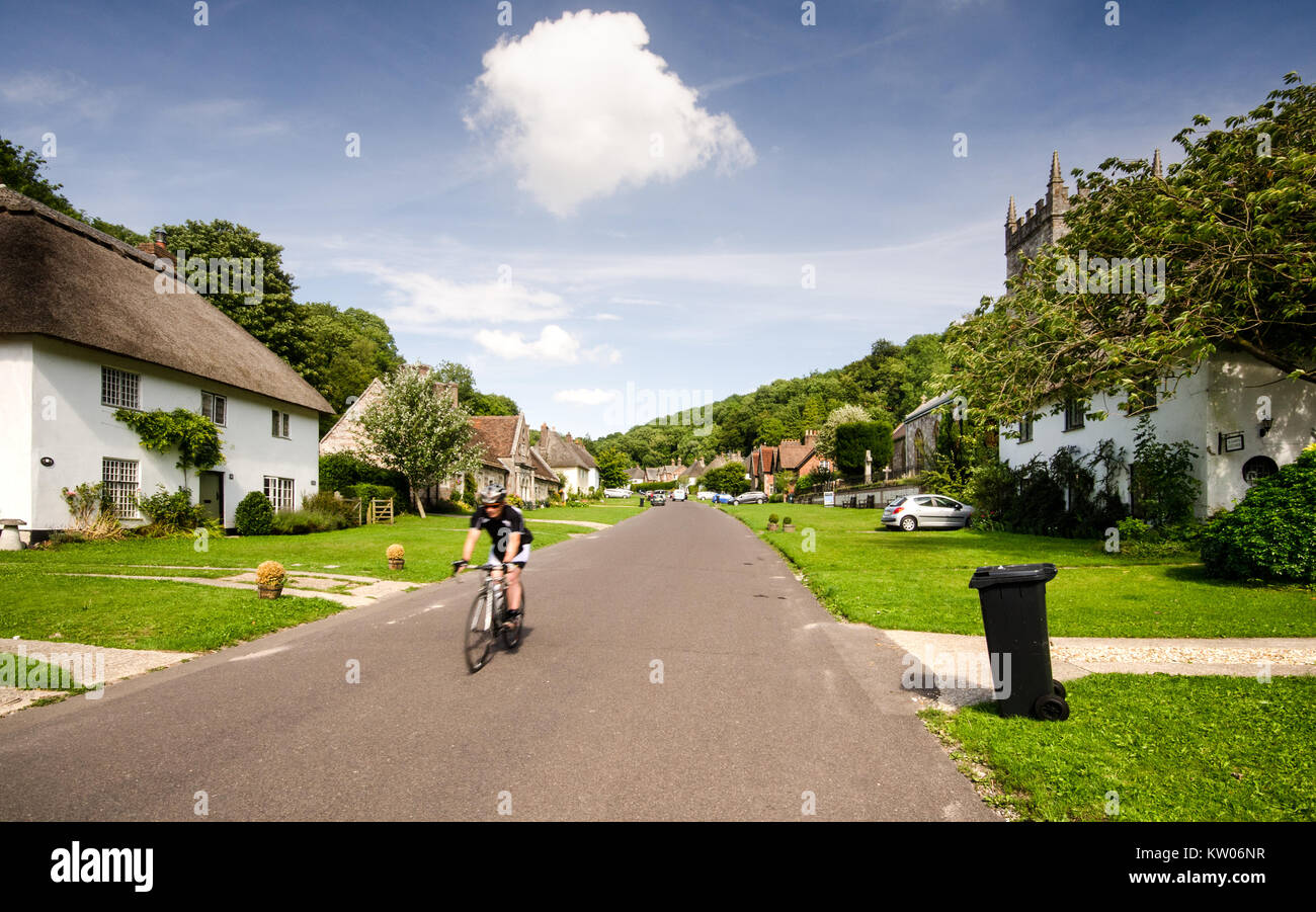 Dorchester, England, UK - 8 août 2013 : Un cycliste descend la rue principale du village pittoresque de Milton Abbas, bordée de chaume traditionnels Banque D'Images
