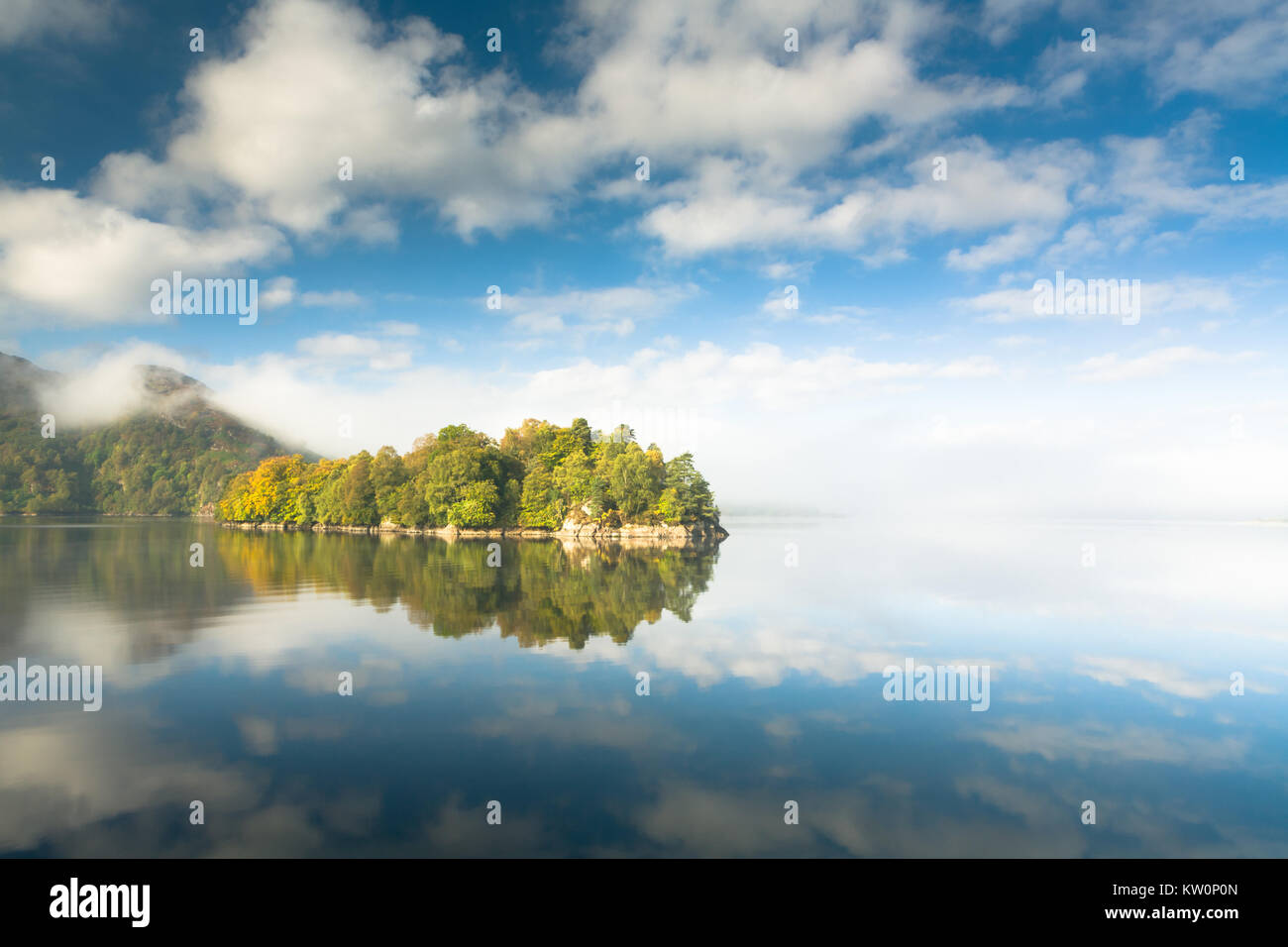 Îles boisées en automne pontés réfléchir avec ciel bleu et nuages blancs dans un miroir encore Loch Katrine, Perthshire, Écosse Banque D'Images