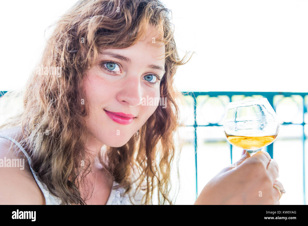 Closeup portrait d'un happy smiling young woman holding bourbon rhum boisson alcoolisée en main par l'eau dans un restaurant d'été Banque D'Images
