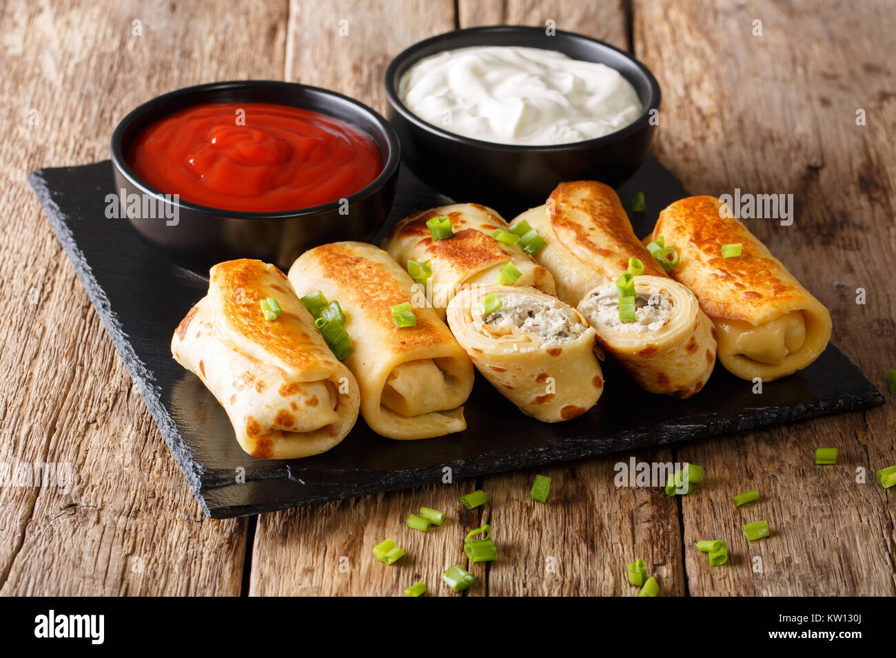 Rouleaux de crêpes délicieux avec du poulet, du fromage et des champignons close-up et les sauces sur la table horizontale. Banque D'Images