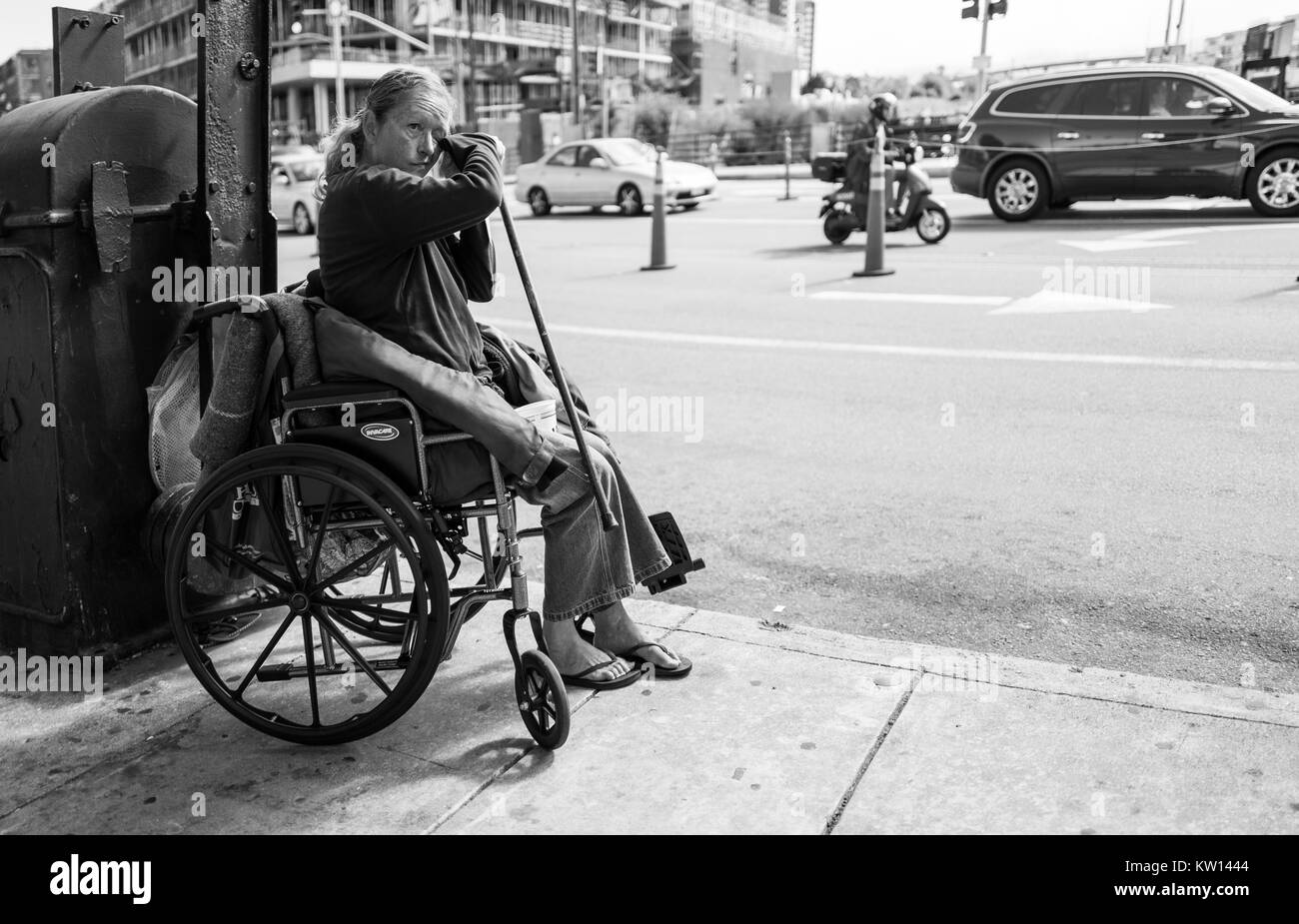 Portrait noir et blanc d'une femme sans-abri dans un fauteuil roulant avec une canne et essuyant son visage, dans le bassin de la Chine quartier de San Francisco, Californie, 2016. Banque D'Images