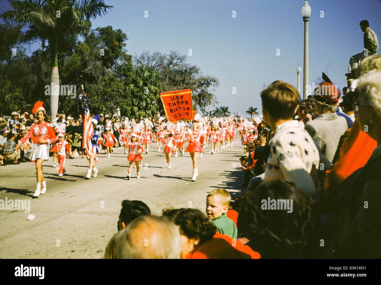 Spectateurs watch en tant que membres de l'Université de Tampa Club Baton parade le long d'une rue en uniforme, avec un drapeau américain, Tampa, Floride, 1952. Banque D'Images