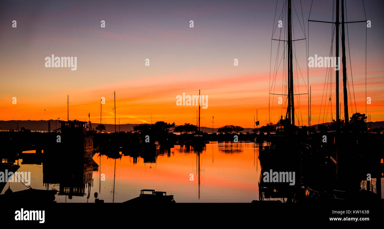 Un coucher du soleil se reflète dans l'eau marina avec silhouettes de voiliers et leurs mâts. Banque D'Images