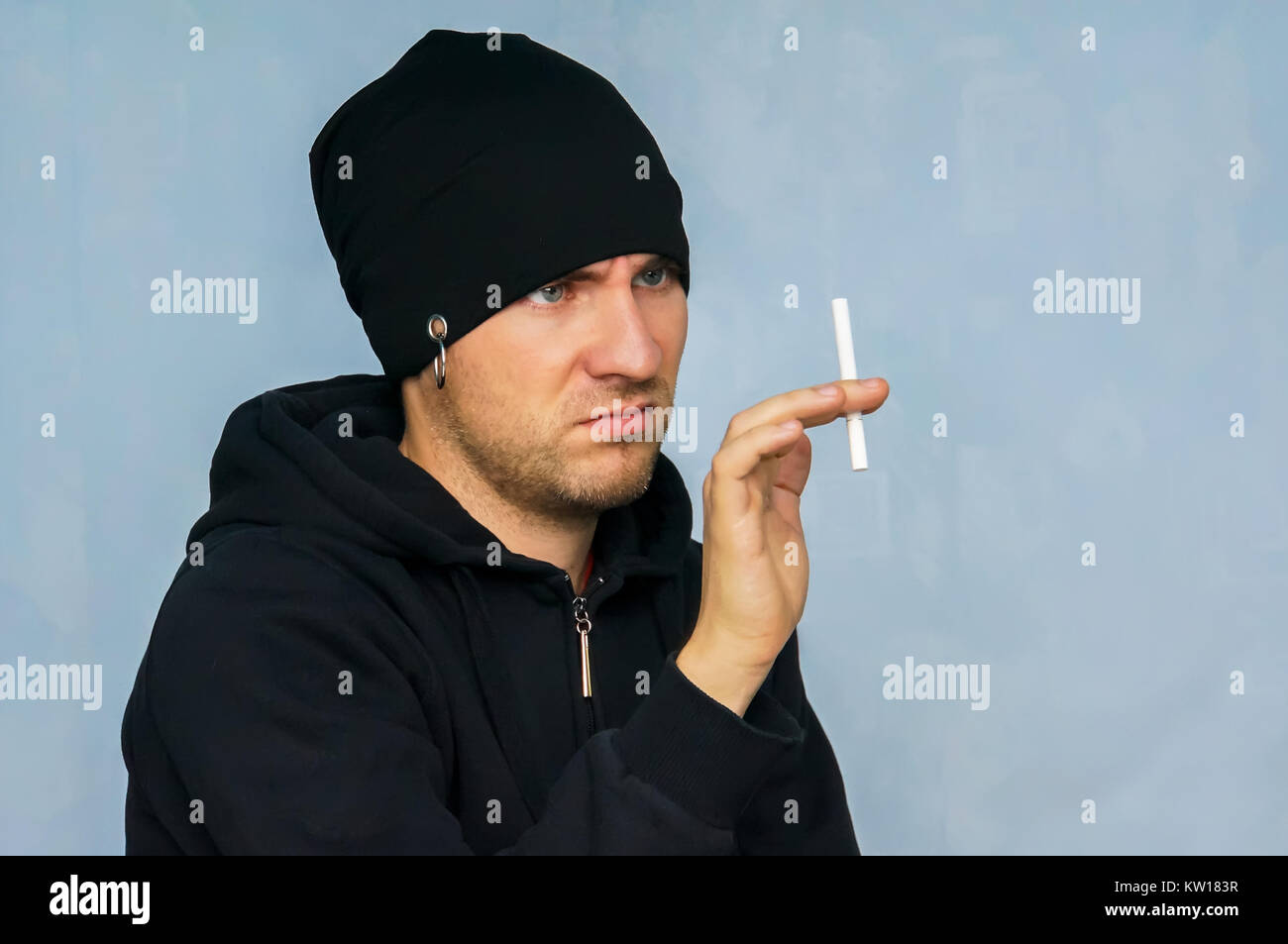 Un jeune homme en vêtements pour les jeunes sous-culture tenant une cigarette. Dégoûté par le tabagisme. Pour cesser de fumer. L'aversion pour la fumée de tabac. La lutte contre l'Smok Banque D'Images