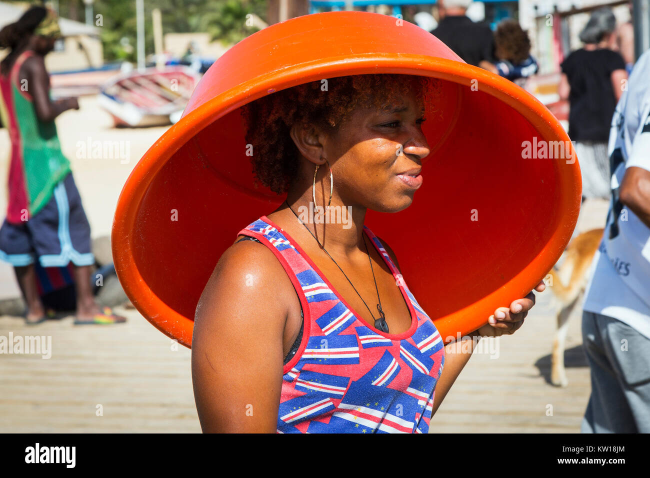 Jeune femme à Santa Maria portant un tee shirt avec le drapeau national du Cap-Vert comme modèle, s'abritant sous un bassin en plastique orange à partir de la st Banque D'Images