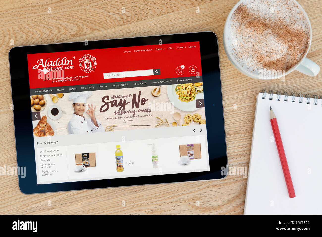 L'Aladdin Street site sur un iPad tablet device qui repose sur une table en bois à côté d'un bloc-notes et un crayon et une tasse de café (rédaction uniquement) Banque D'Images