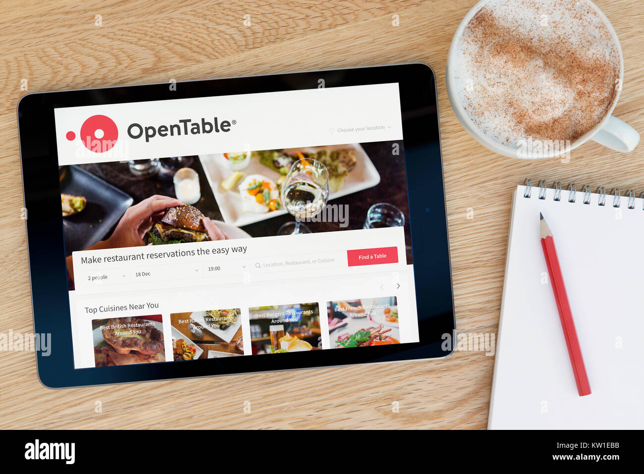 La table ouverte site sur un iPad tablet device qui repose sur une table en bois à côté d'un bloc-notes et un crayon et une tasse de café (rédaction uniquement) Banque D'Images