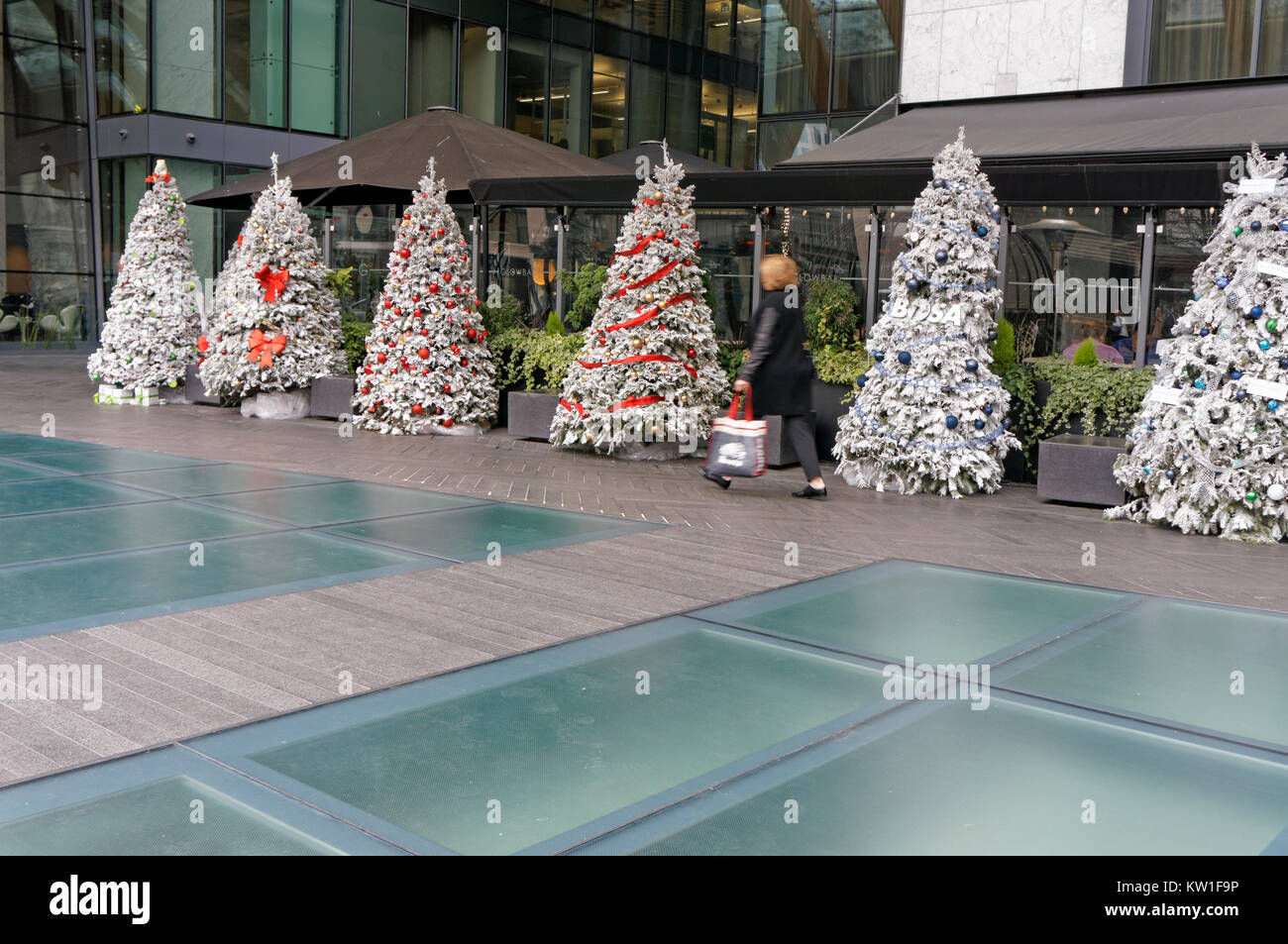 Femme transportant un sac shopping en passant devant une rangée d'arbres de Noël artificiels dans le centre-ville de Vancouver, BC, Canada Banque D'Images