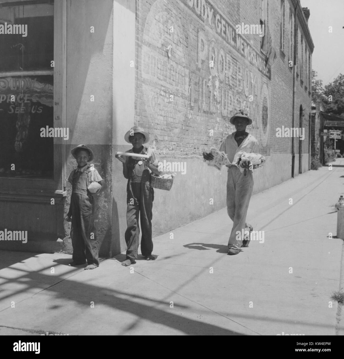 Les jeunes garçons se tiennent sur un trottoir par un immeuble commercial détenant divers produits, en Port Gibson, Mississippi, Août, 1940. Banque D'Images