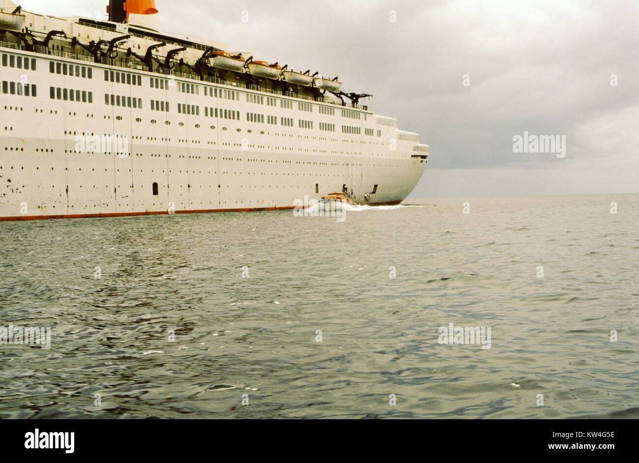 Partie arrière de la ligne Cunard Queen Elizabeth 2 bateau de croisière, avec un petit bateau à moteur qui approche, en mer, 1975. Banque D'Images