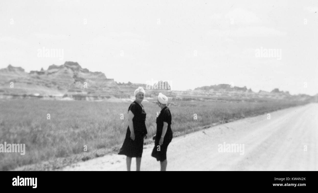 Deux touristes femelles adultes portant des robes noires assorties et turbans blancs se tiennent sur une route à côté de mesas, South Dakota, United States, 1958. Banque D'Images