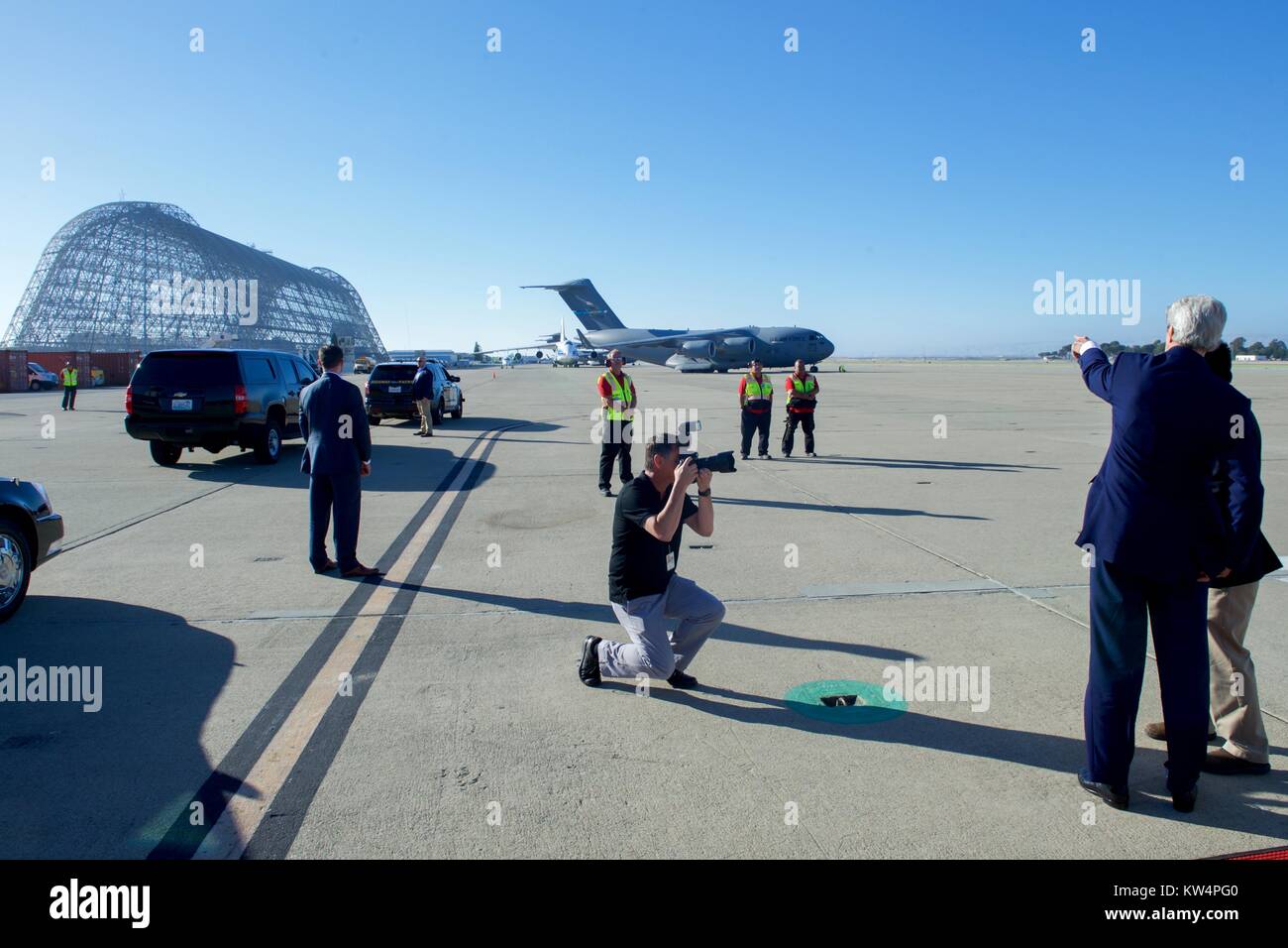 Le secrétaire d'Etat américain John Kerry pointe vers le squelette de Hangar One après l'atterrissage à Moffett Field à Mountain View, Californie, à la suite d'un vol de Andrews Air Force Base à Camp Springs, Maryland, ainsi il peut assister à des événements autour de l'entreprise mondiale Sommet mondial à l'Université de Stanford à Palo Alto, Californie, le 22 juin 2016. Image courtoisie du département d'Etat. Banque D'Images