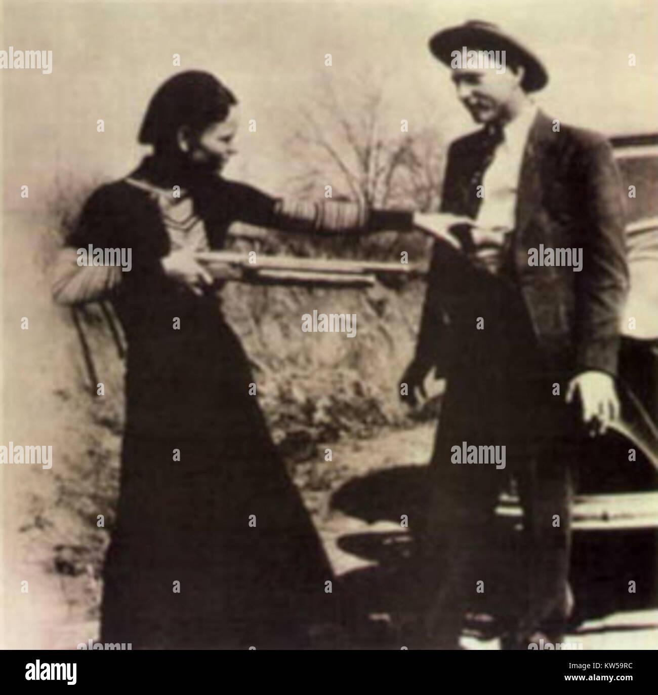 Une photographie de Bonnie Parker visant de manière ludique Clyde Barrow avec un fusil de chasse, capturant un moment de légèreté entre le célèbre duo criminel. Bonnie et Clyde étaient tristement célèbres pour leurs vols de banque et leurs activités criminelles au début des années 1930 aux États-Unis. Cette image contraste leurs tristement célèbres vies criminelles avec un moment d'interaction informelle. Banque D'Images