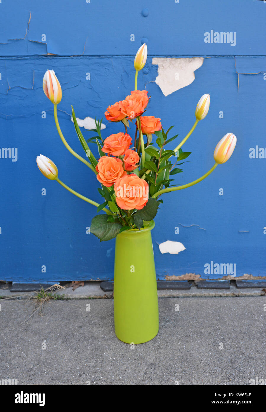 Grand arrangement de roses orange et tulipes dans un vase vert sur un fond de peinture bleue de déroulage. Banque D'Images