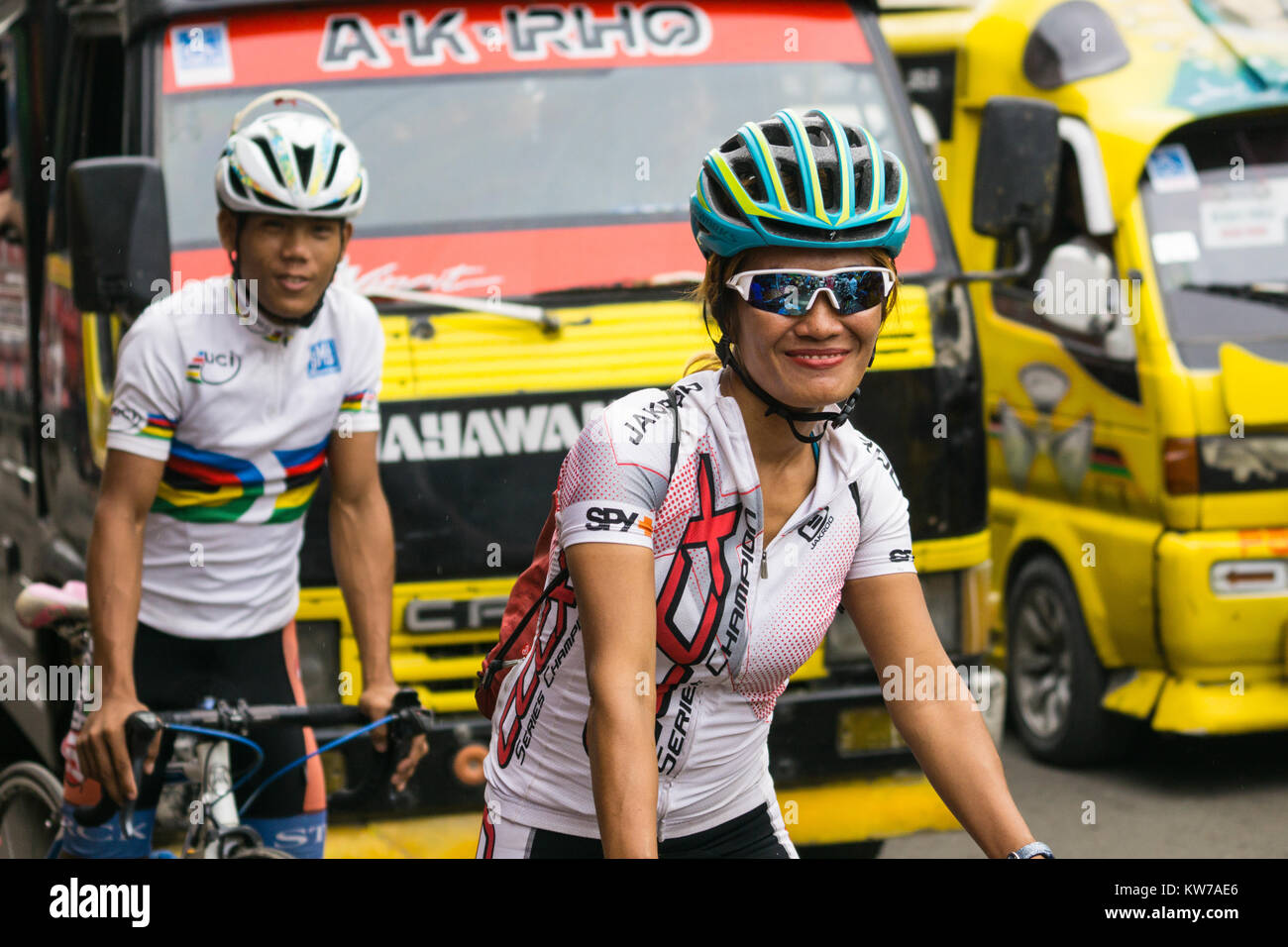 A smiling woman cycling with companion le long d'une rue animée à l'intérieur de la ville de Cebu, Philippines Banque D'Images