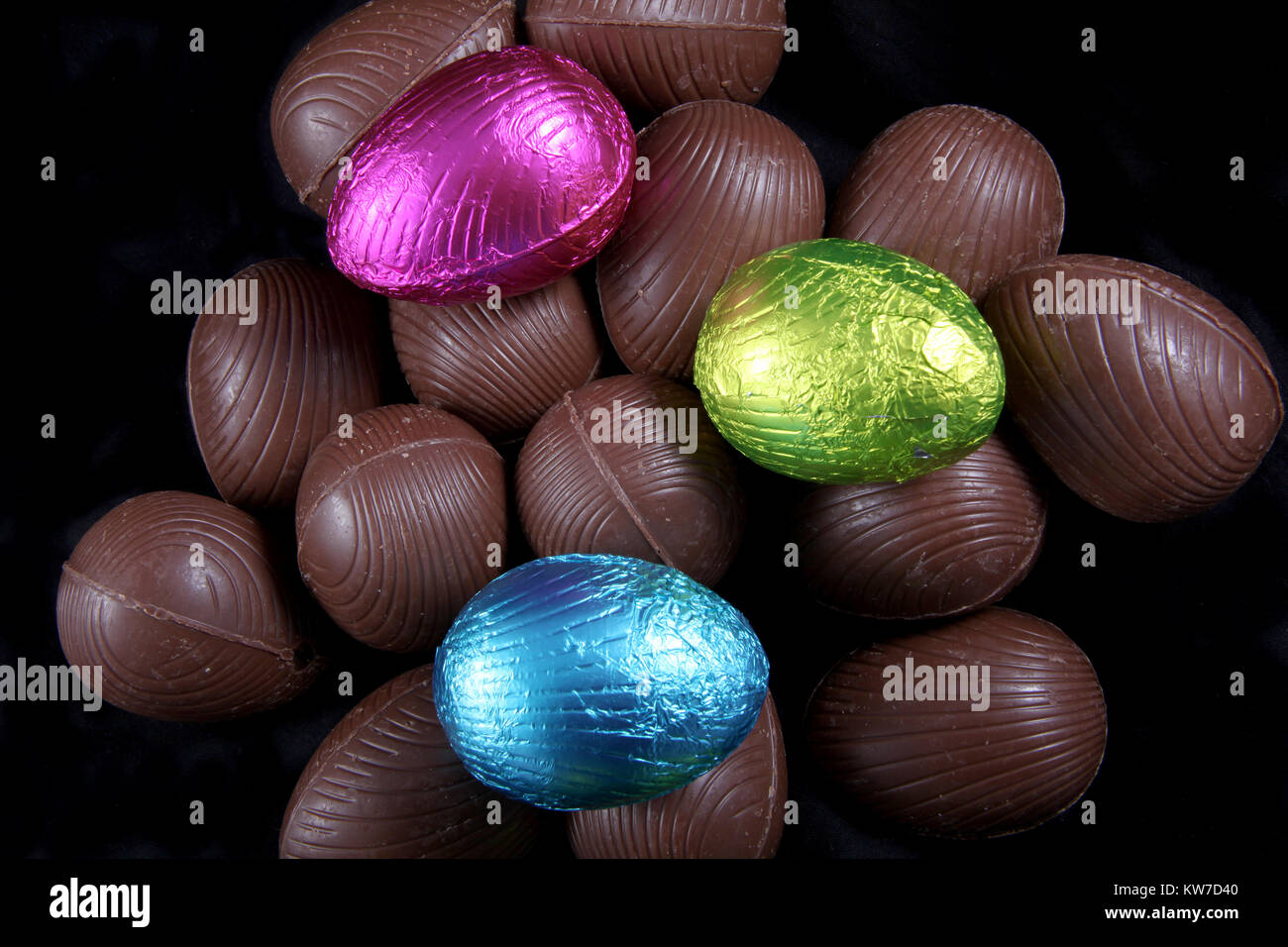 Pile de papier aluminium enveloppé & unwrapped chocolate Easter eggs en rose, bleu et vert citron, sur un fond noir. Banque D'Images