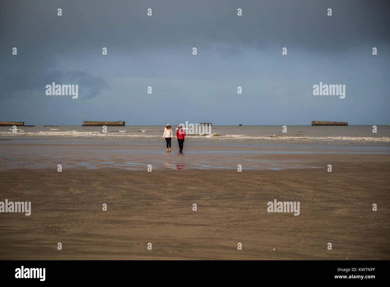 Marcher le long de la plage à Arromanches les Bains avec le reste de la Phoenix caissons dans l'arrière-plan. Banque D'Images