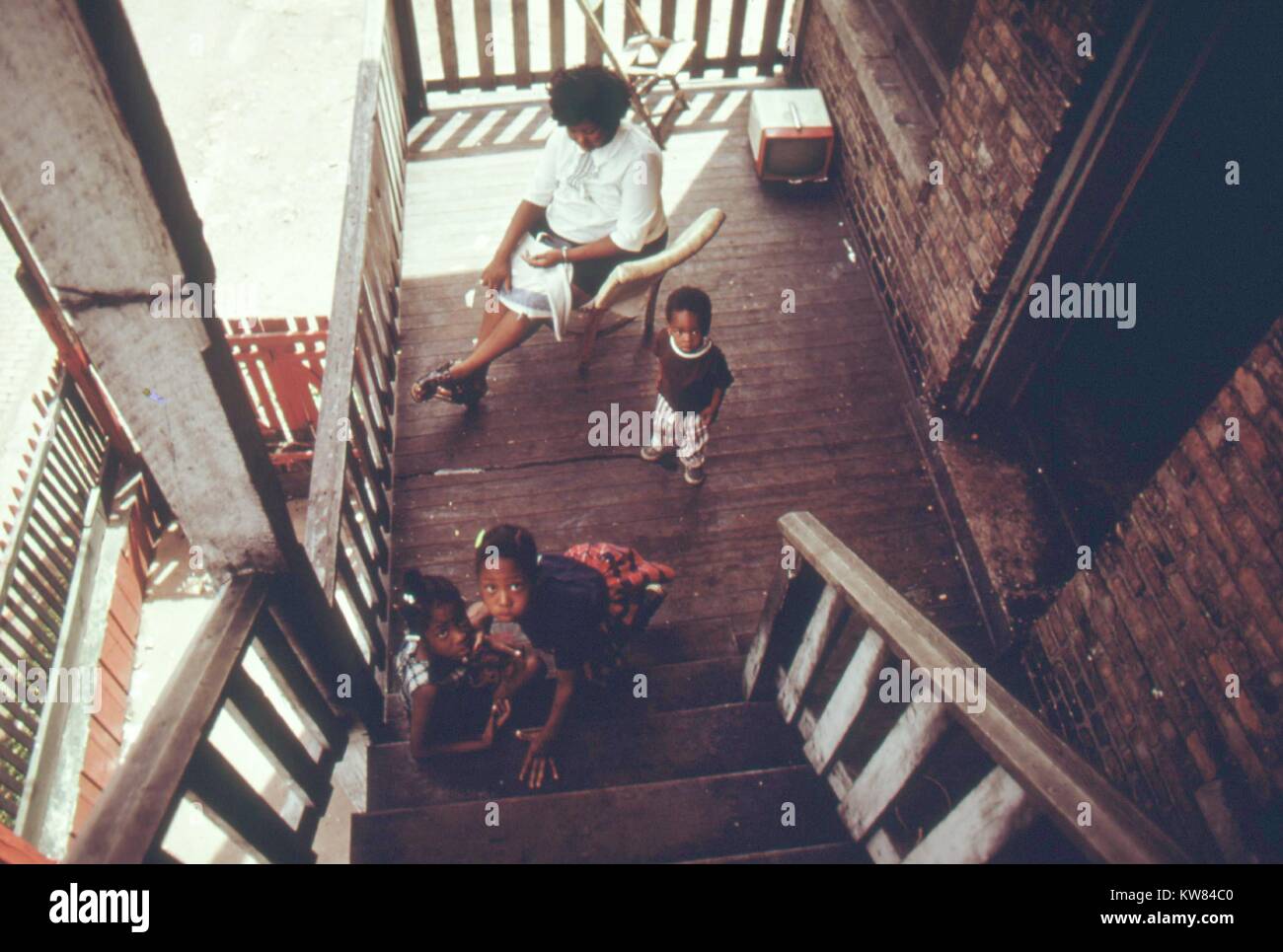 Les logements anciens dans la communauté noire de Chicago, côté ouest avec trois enfants jouant sur le porche comme une mère est assise à côté d'eux, Chicago, Illinois, 1973. Image courtoisie John White/US National Archives. L'image de courtoisie des Archives nationales. Banque D'Images