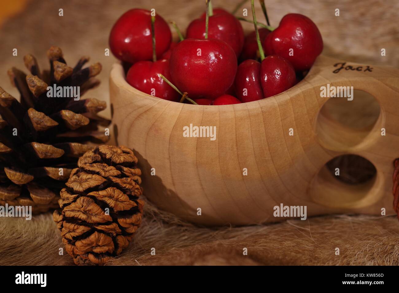 Les cerises dans une coupelle en bois finlandais Kulsa sur une fourrure de renne avec cocottes. La vie encore scandinaves et la saine alimentation. L'hiver 2017. Banque D'Images
