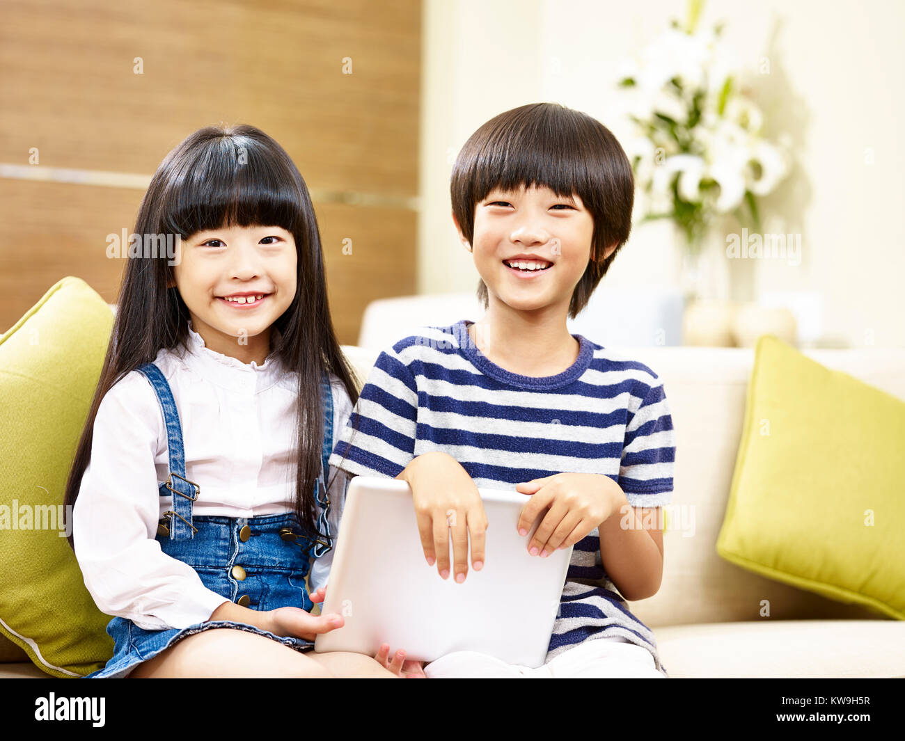 Deux enfants asiatiques mignon petit garçon et petite fille assise sur la table holding digital tablet smiling at camera Banque D'Images
