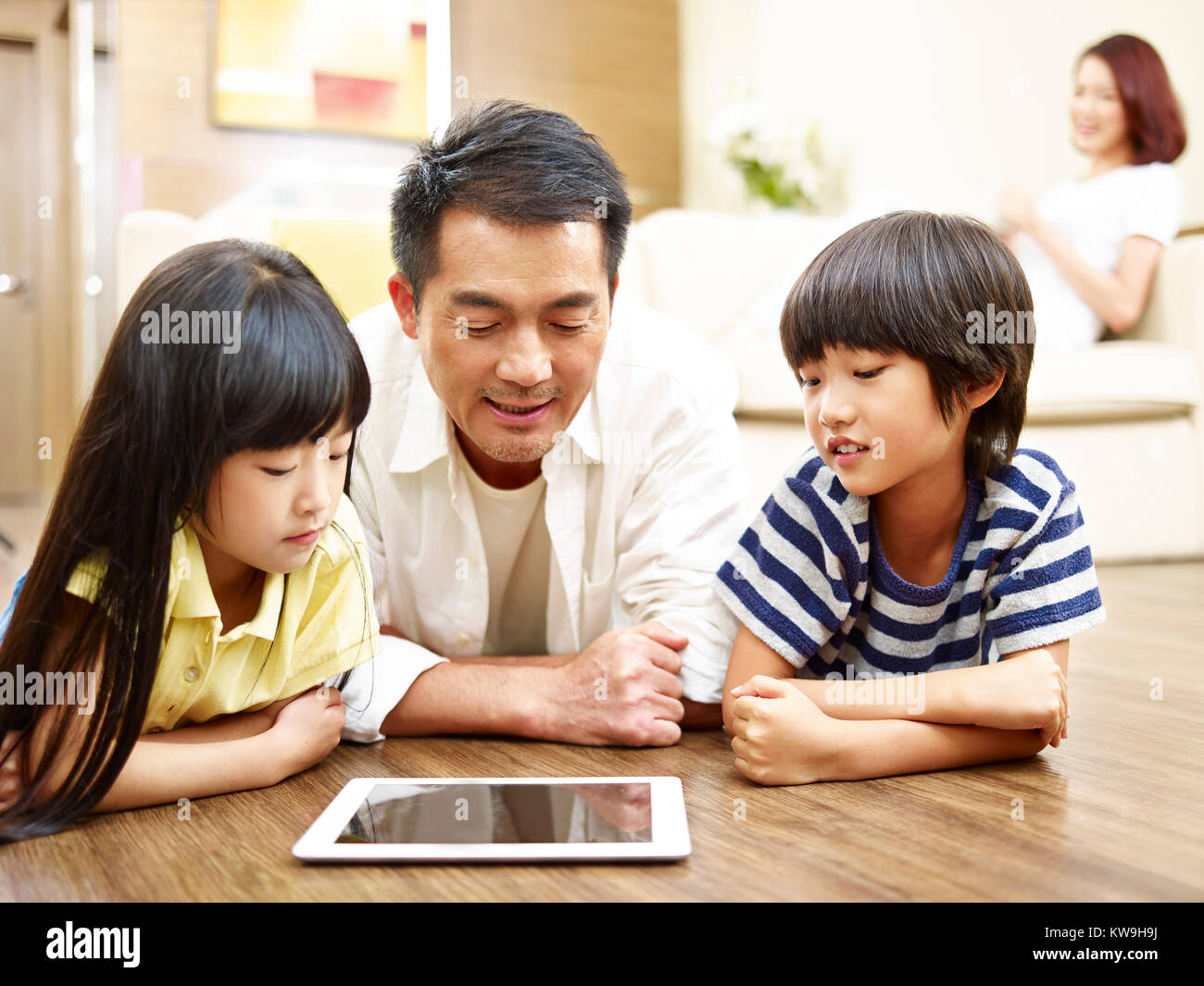 Mère de deux enfants d'Asie et de marbre jouant avec tablette numérique alors que mère regardant en arrière-plan. Banque D'Images