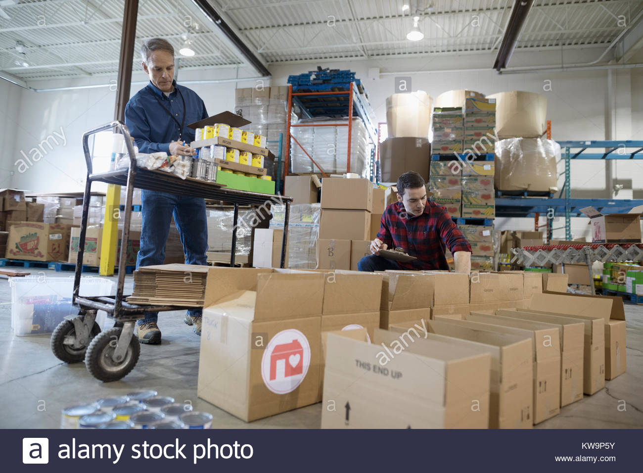 Hommes bénévoles avec de la nourriture en conserve le remplissage des boîtes de dons dans l'entrepôt Banque D'Images