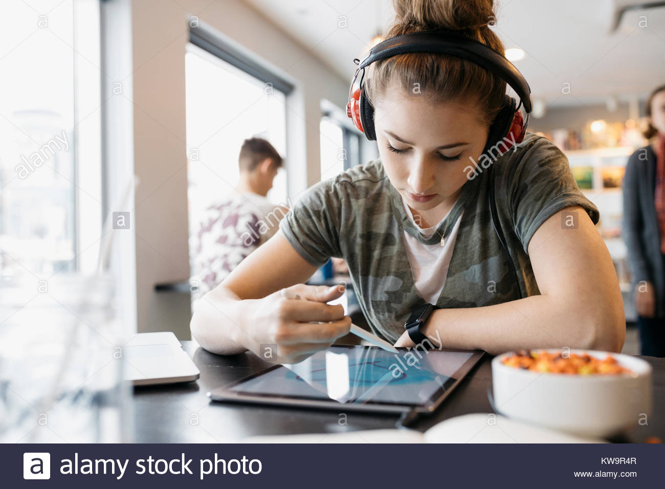 High school girl étudiant avec l'aide d'écouteurs stylet,dessin sur digital tablet in cafe Banque D'Images