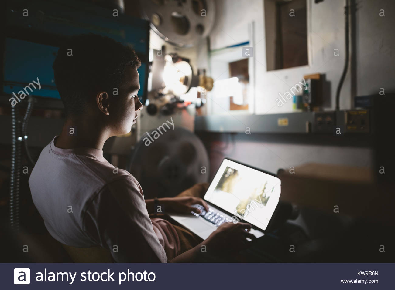 Tween mixed race boy using laptop in projectionniste de cinéma sombre Banque D'Images