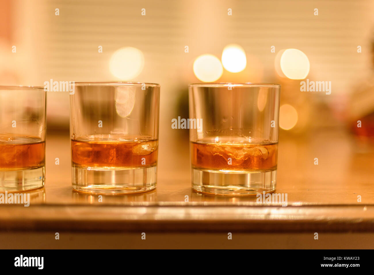 Gros plan du bourbon whiskey verres avec de la glace se sont alignées sur la table en bois avec des bougies en arrière-plan Banque D'Images