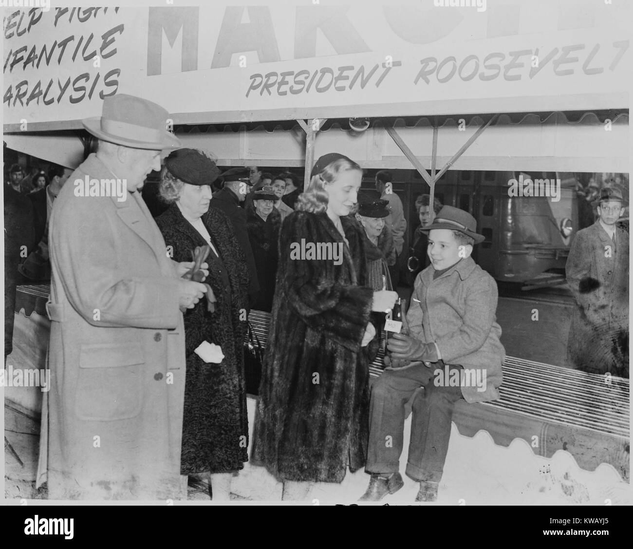 Margaret Truman, fille du président Harry Truman et la Première Dame Bess Truman, gouttes une pièce de monnaie dans une bouteille tenue par un jeune garçon lors d'une apparition publique de la March of Dimes, le 14 janvier 1946. Banque D'Images