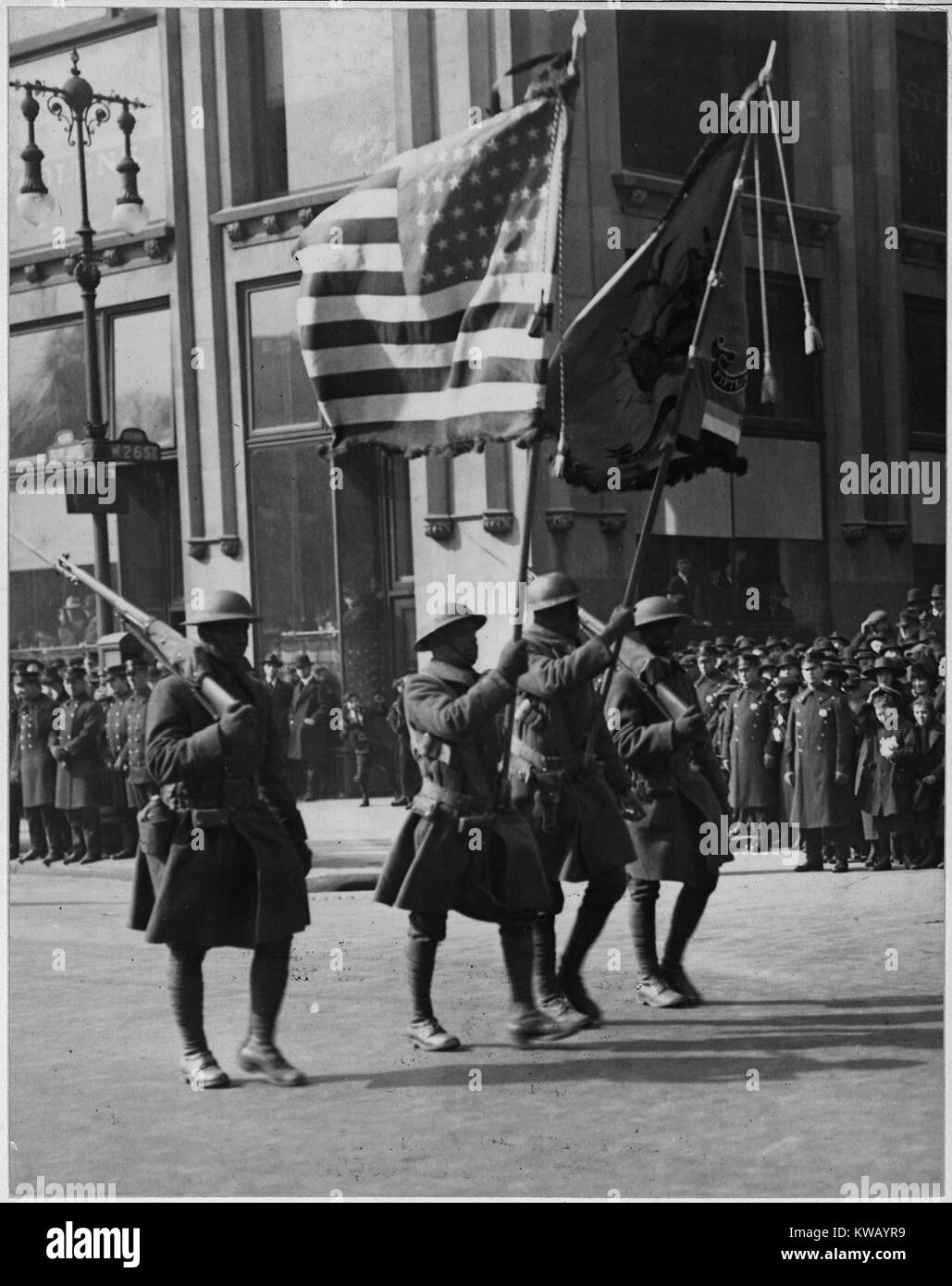 Quatre hommes africains-américains en uniforme à pied en formation dans la rue portant des drapeaux et des armes à feu lors d'un défilé pour la célèbre 369e Infantry, à son retour de France, New York, New York, 1919. L'image de courtoisie des Archives nationales. Banque D'Images