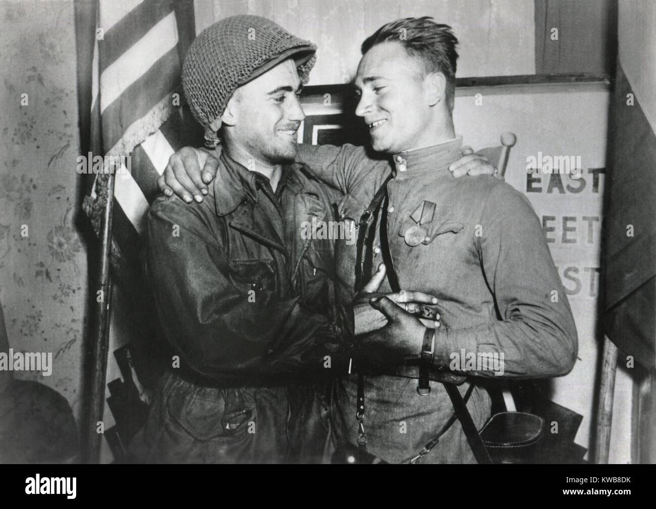 Le lieutenant américain William Robertson et Alexander Sylvashko embrasser le lieutenant soviétique. Derrière eux est un signe, 'East Meets West' pour célébrer la réunion de l'URSS (Russe) et les armées américaine, près de Torgau, Allemagne. Le 25 avril 1945. La Seconde Guerre mondiale 2. (BSLOC 2014 8 79) Banque D'Images