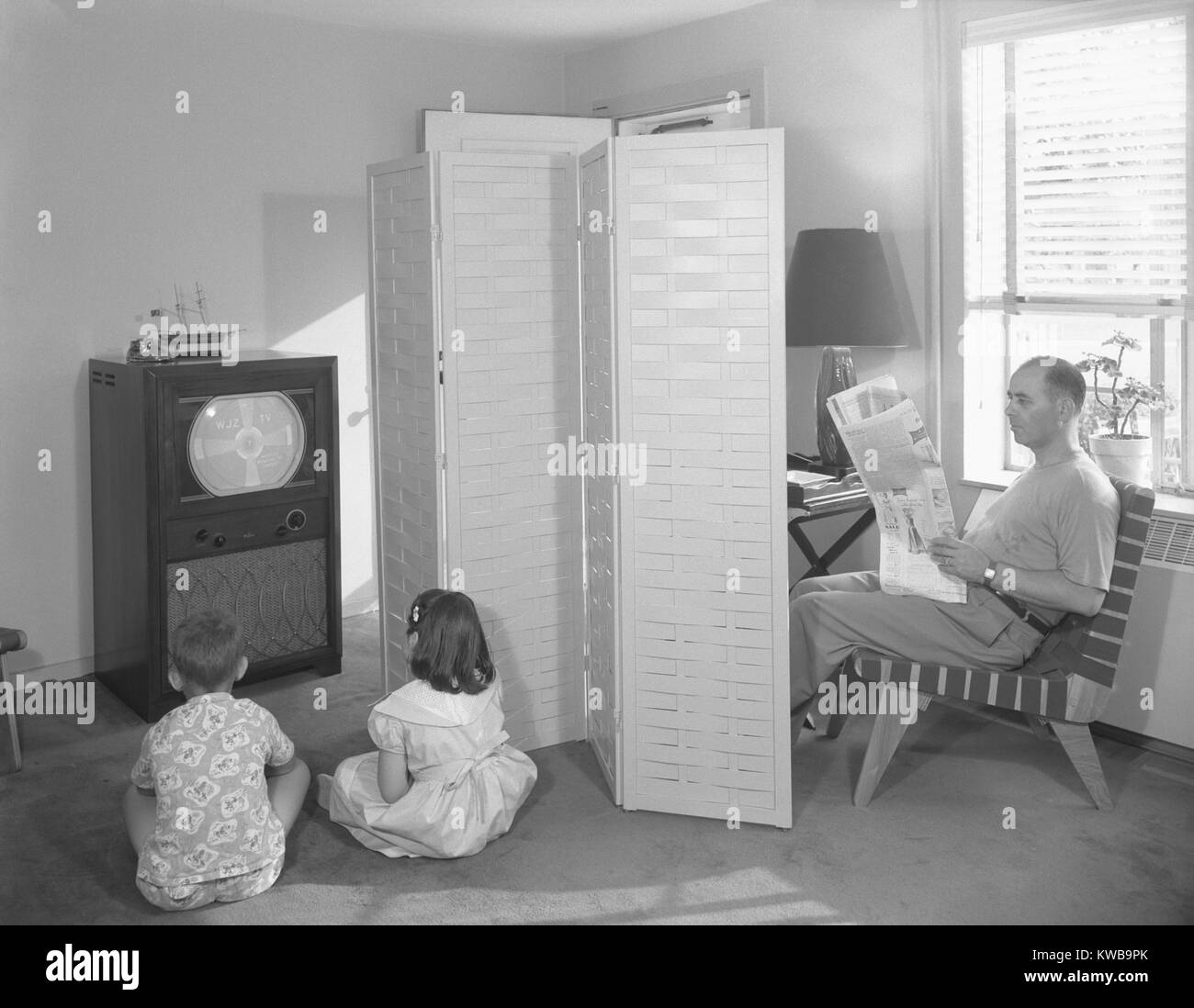 Père lisant le journal, tandis que deux enfants d'anticiper le début de la télévision. Dans un appartement de la ville de New York, le téléviseur affiche un modèle de test avant de commencer sa journée de radiodiffusion. Le 12 juillet 1950. (BSLOC   162 13 2014) Banque D'Images